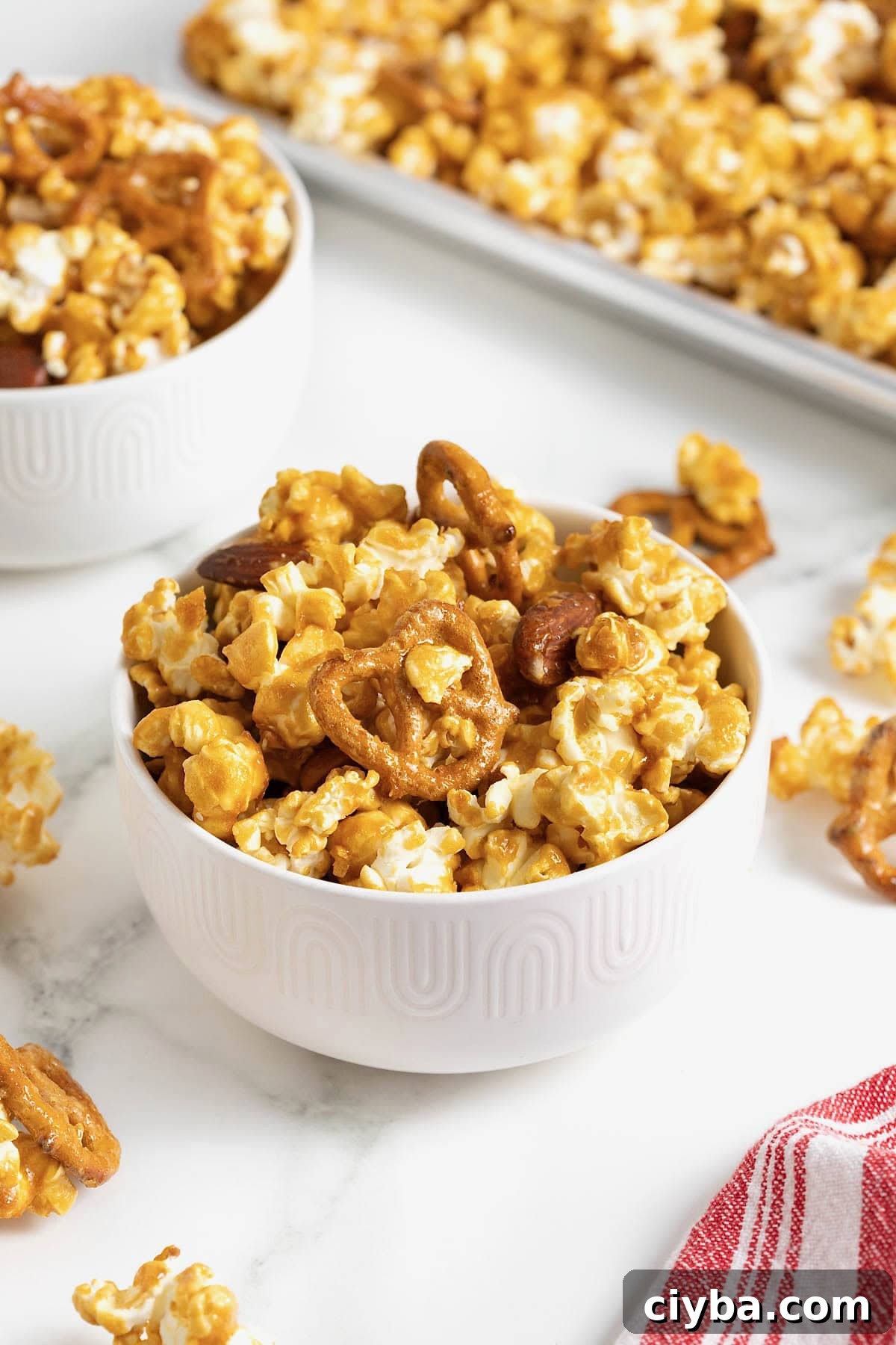 A bowl of caramel corn mixx in a small white bowl on a white marble counter.