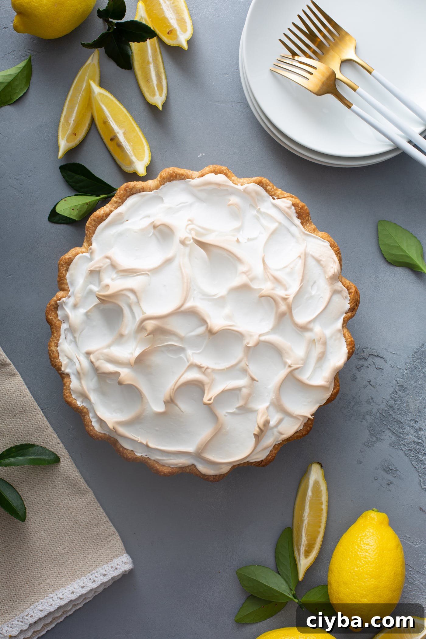 A lemon meringue pie with fluffy browned meringue and lemon wedges