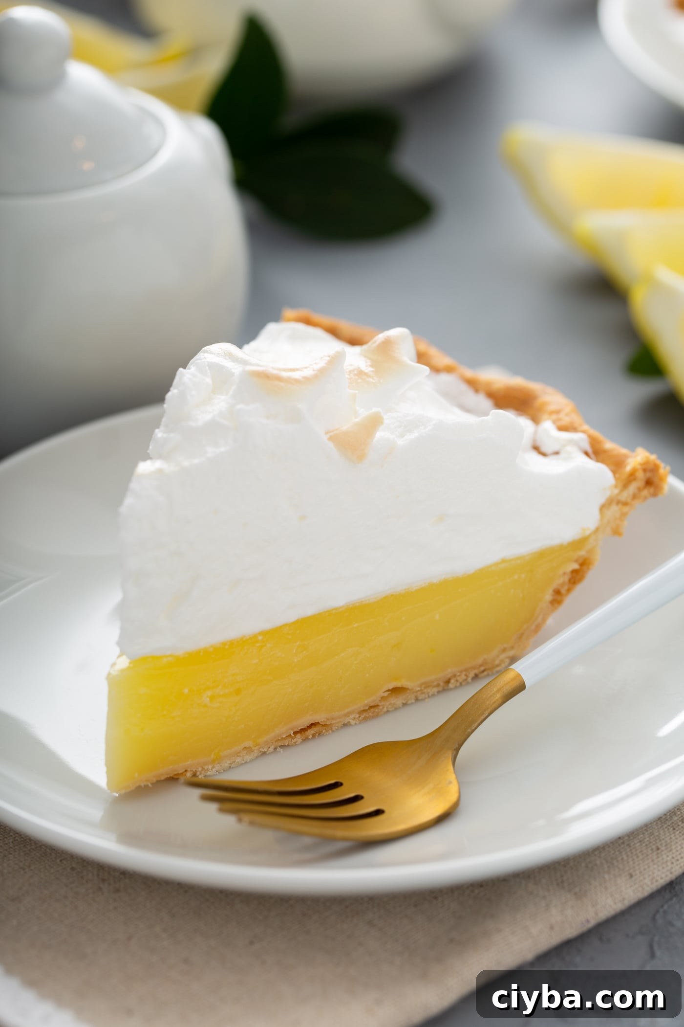 A slice of lemon meringue pie on a white plate with a fork