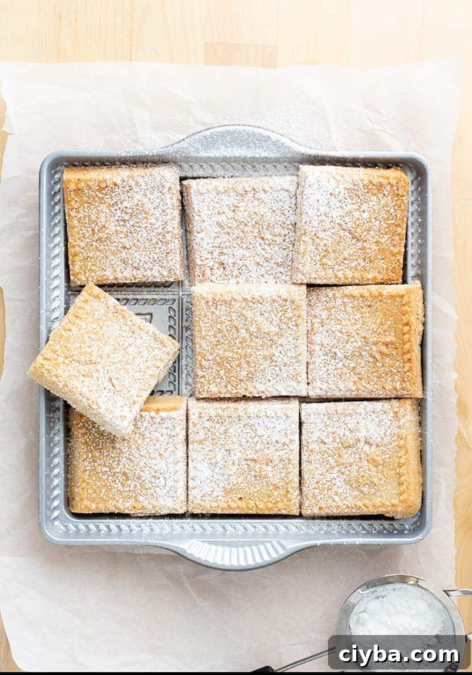 Overhead image of cut shortbread squares in pan with powdered sugar on white paper