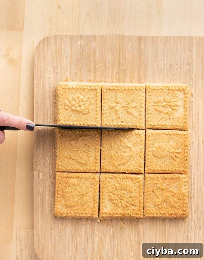 Hand holding a knife cutting apart squares of shortbread on cutting board