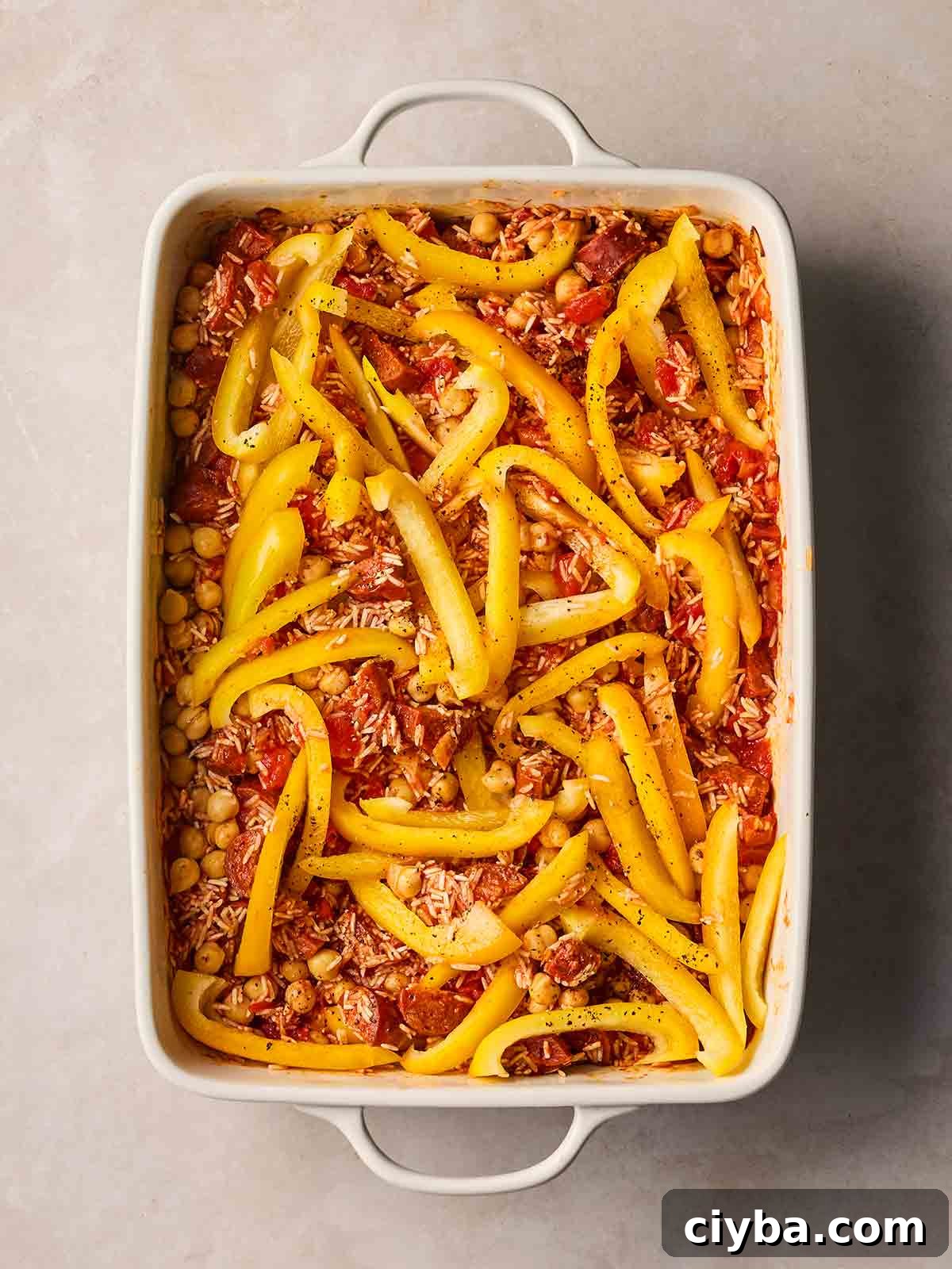 One-Pan Chorizo and Rice Bake: Dump, Bake, Serve 6 An oven dish with ingredients in, ready to bake together, including rice, chorizo, onion, chickpeas and sliced yellow peppers.