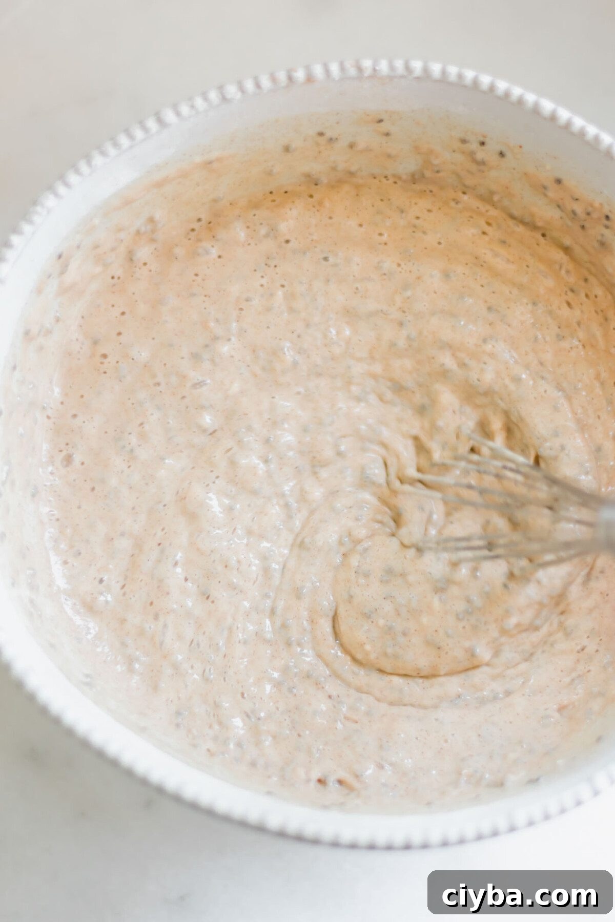 Thick chia seed pancake batter in a glass mixing bowl with a whisk.