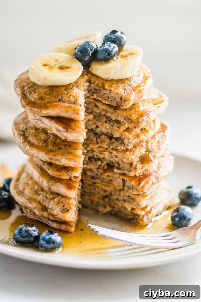 Stack of fluffy pancakes that's been cut into so you can see the inside texture of them. They're topped with blueberries and banana.