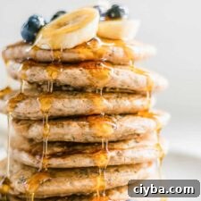 Stack of 7 thick and fluffy chia pancakes topped with maple syrup and blueberries on a plate.