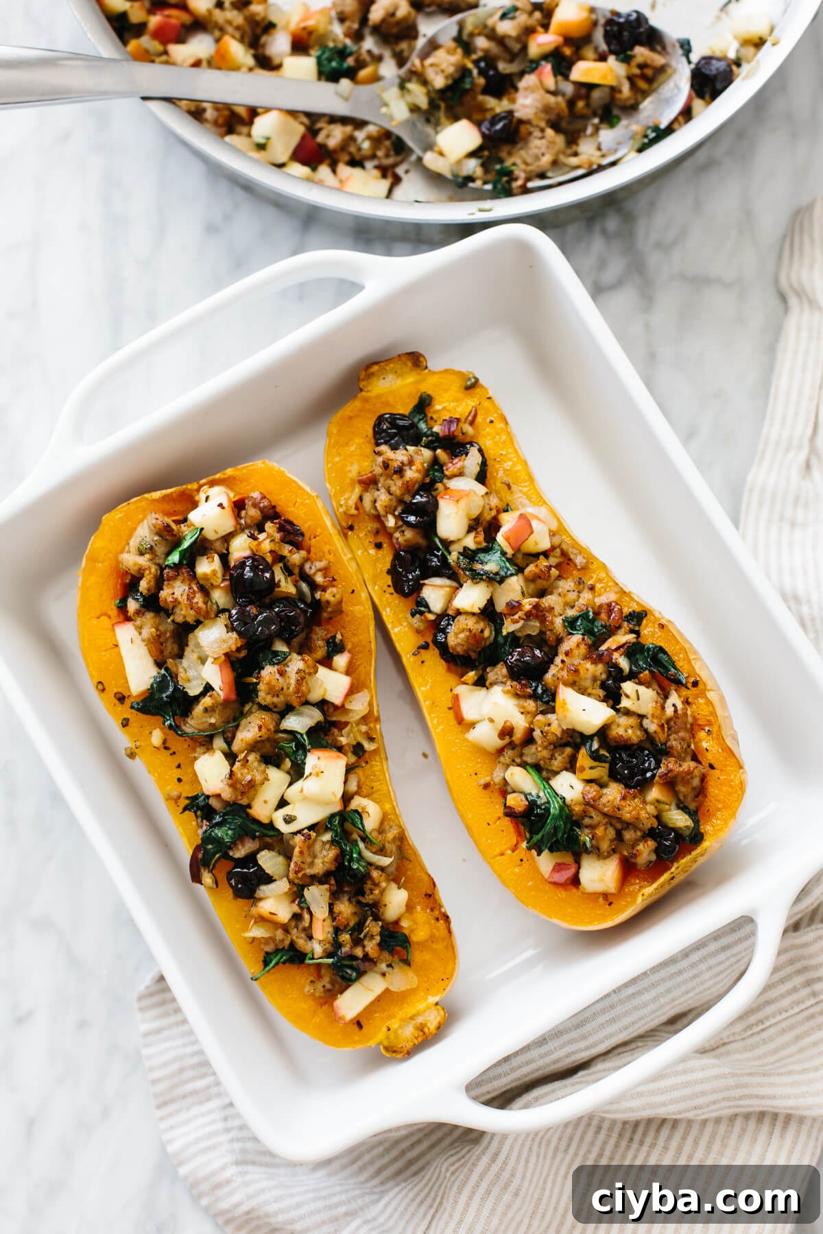 Butternut squash filled with sausage apples and other ingredients in a baking dish.