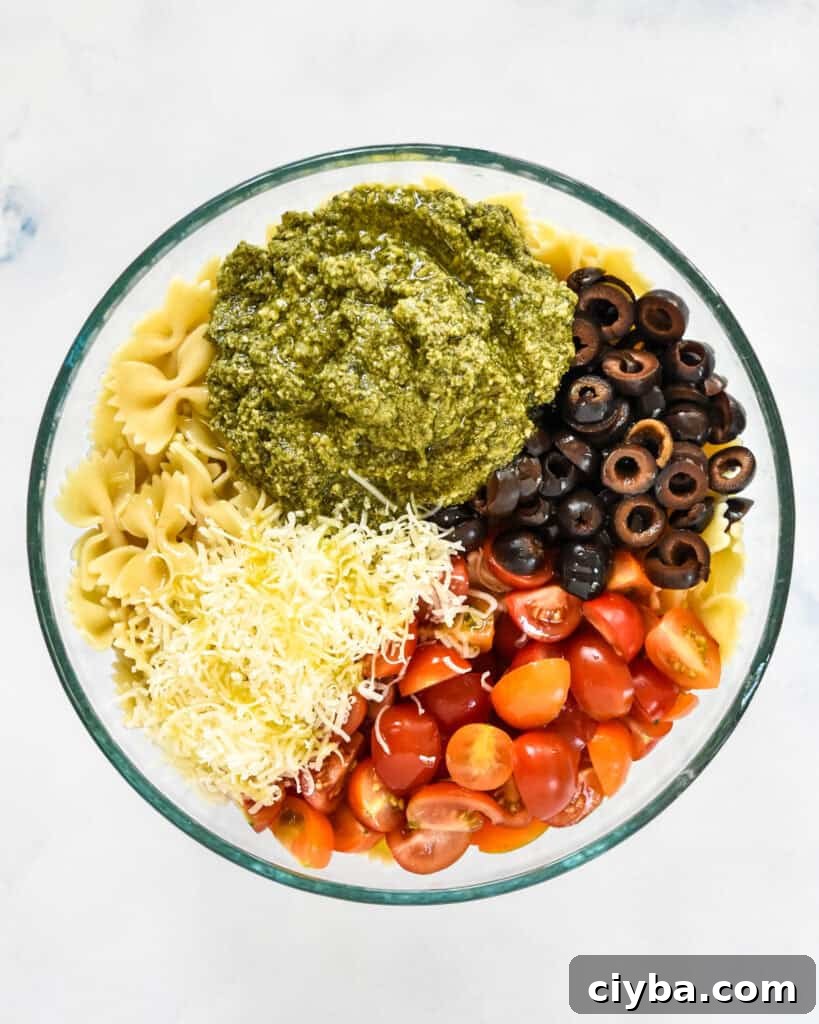 pesto, olives noodles tomatoes and parmesan cheese before stirring the pasta salad.