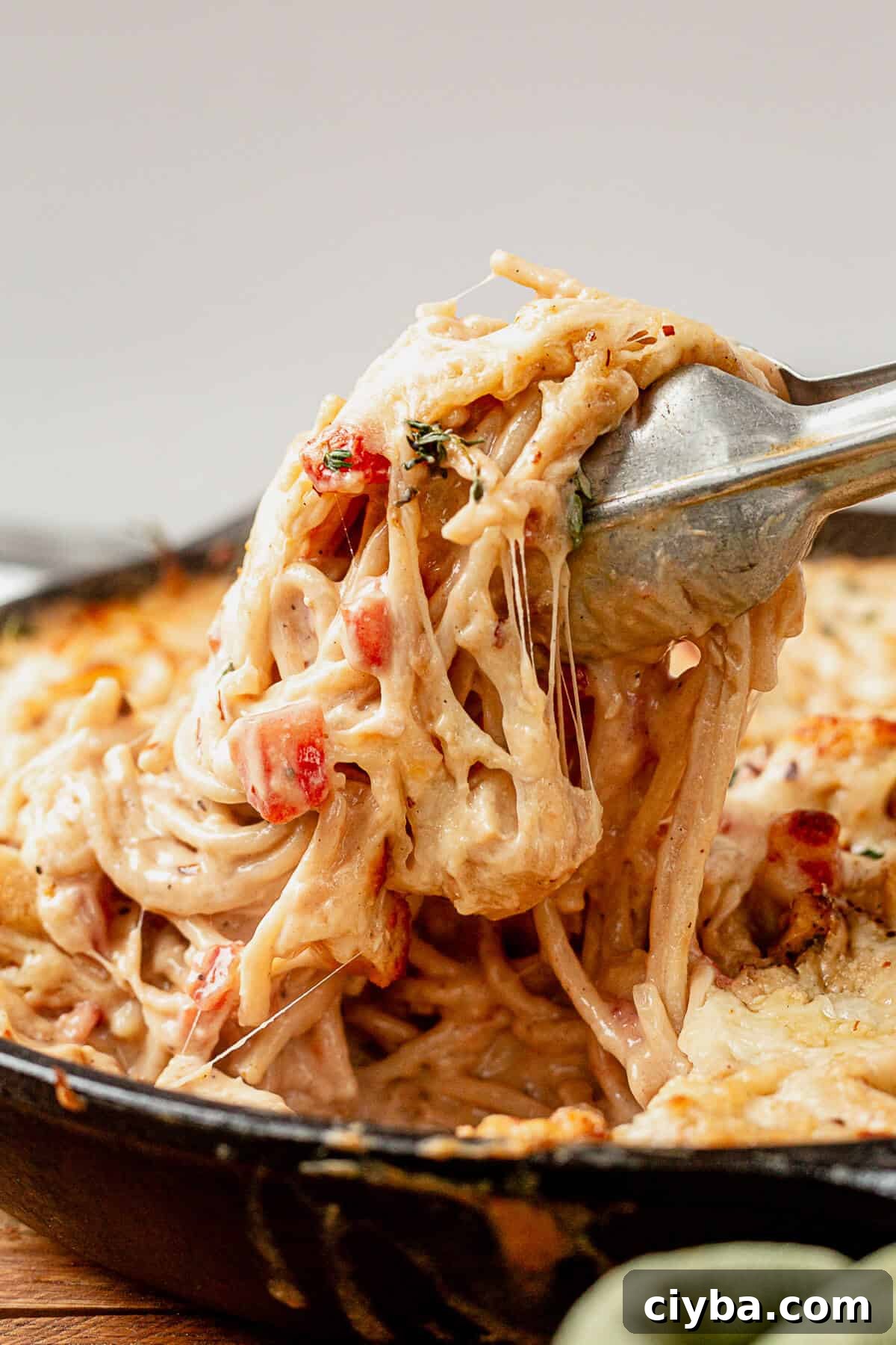 pulling cheesy creamy spaghetti chicken out of a skillet