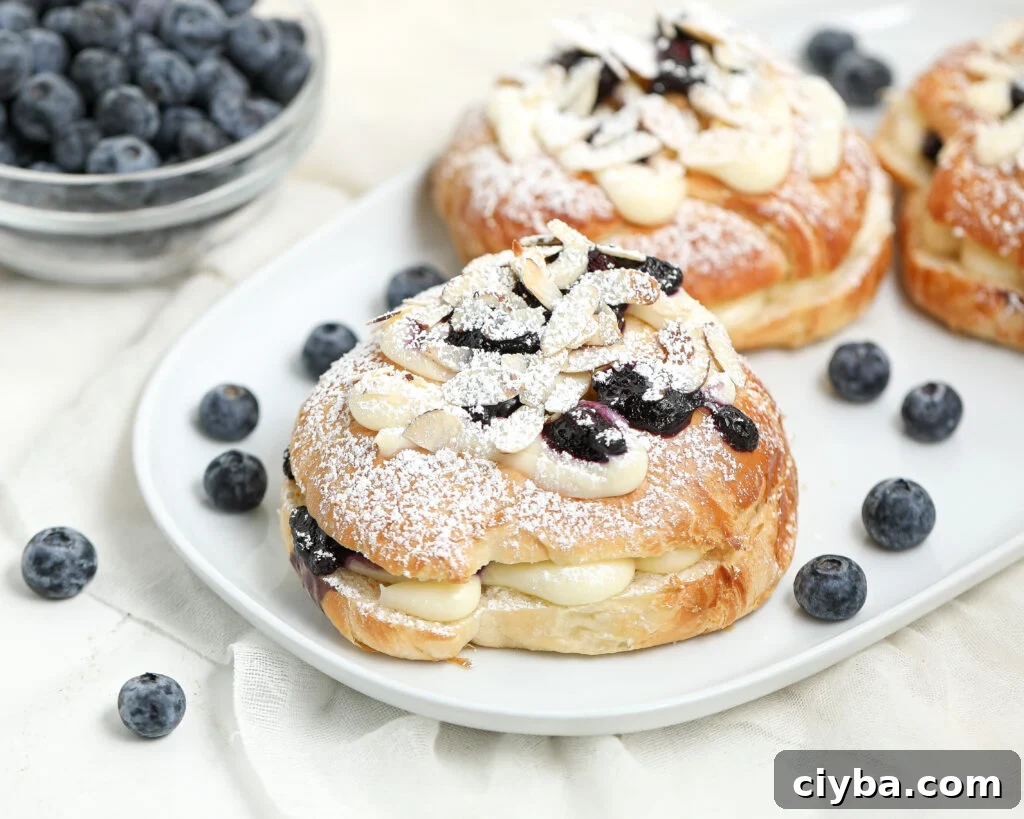 Croissants filled with cheesecake cream and blueberries, topped with sliced almonds and powdered sugar.