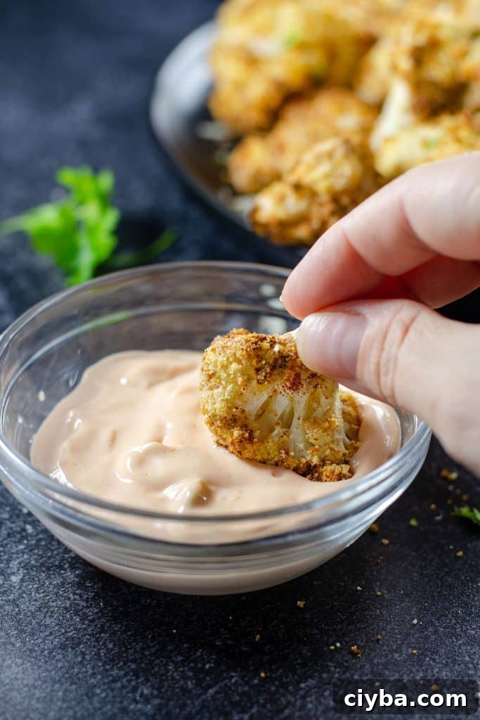 cauliflower floret being dipped in  buffalo dipping sauce