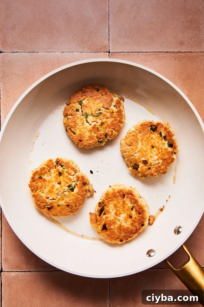 Tuna patties frying in a skillet with crispy golden edges