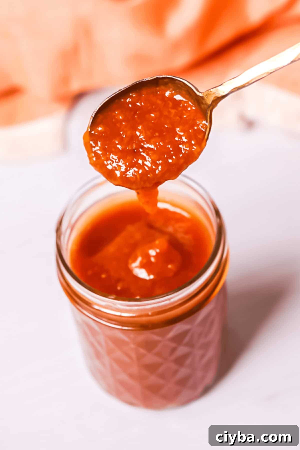 A spoonful of thick, reddish-orange sauce in a jar.
