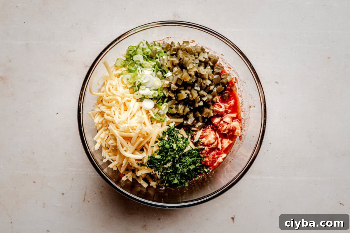 A glass bowl containing shredded cheese, sliced green onions, diced green chiles, diced cooked chicken, and chopped herbs, all arranged in separate sections on a light-colored surface.