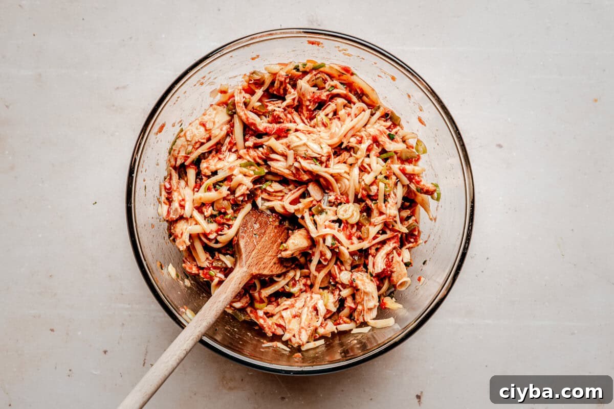 A glass bowl filled with shredded chicken and spices, being mixed with a wooden spoon.