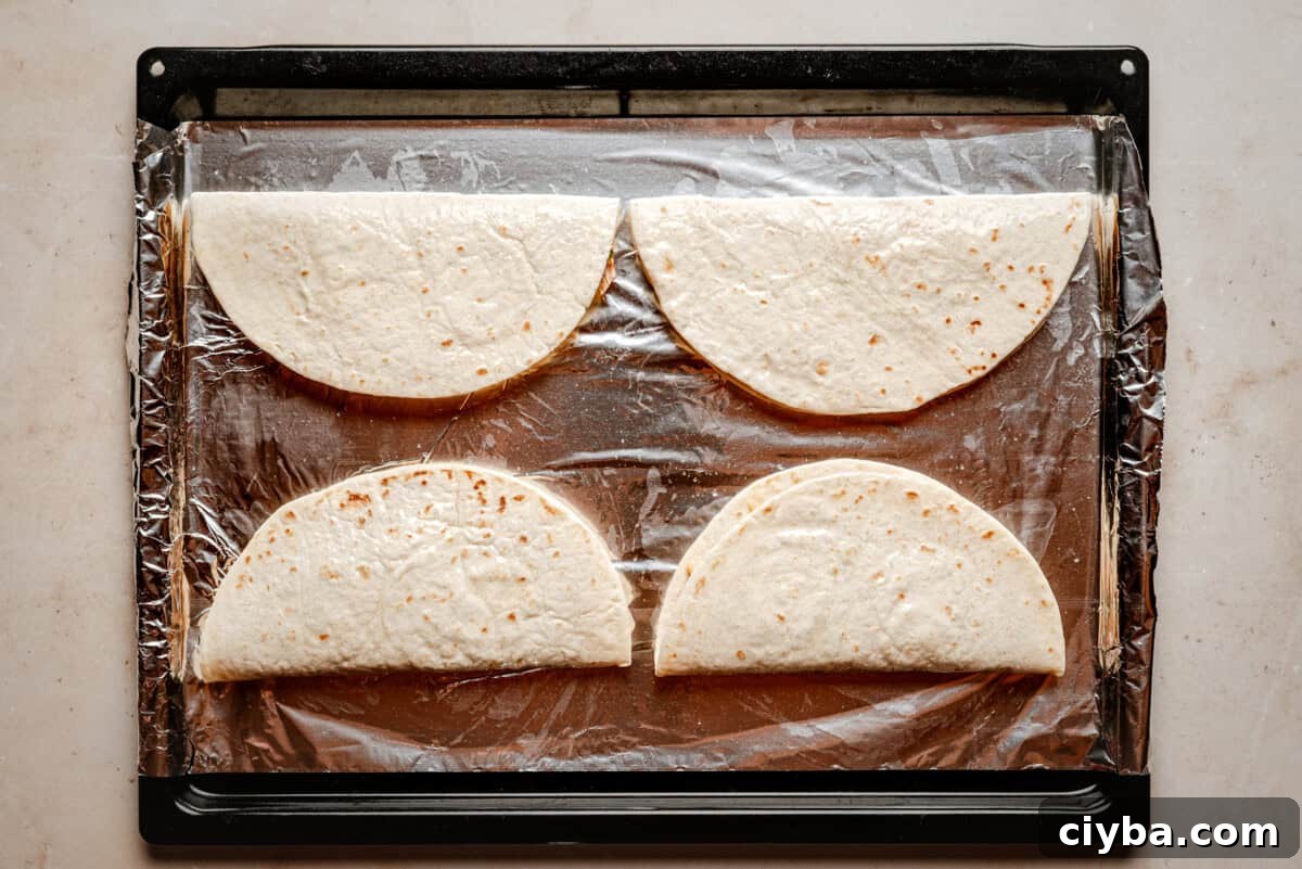 Four folded tortillas are arranged in a single layer on a baking sheet lined with aluminum foil, ready to be cooked.
