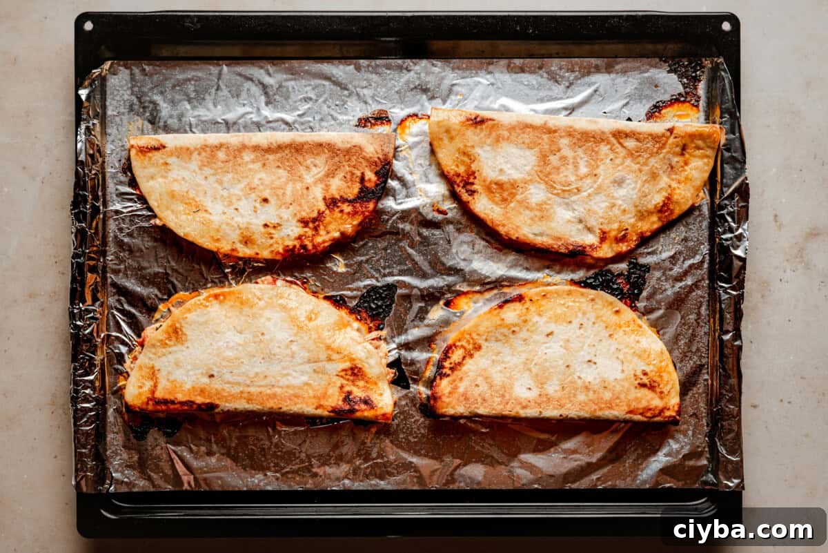 Four golden-brown chicken tinga quesadillas on a foil-lined baking tray, slightly crispy at the edges, resting on a light-colored countertop.