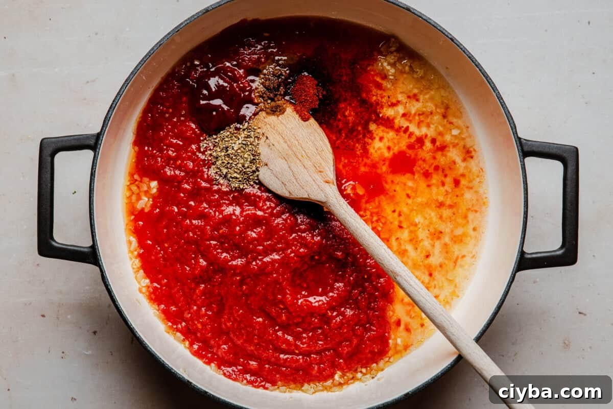 A pot with a wooden spoon contains tomato sauce, minced garlic, oil, and various spices, ready to be mixed together. The ingredients are grouped separately and have vibrant red and yellow colors.