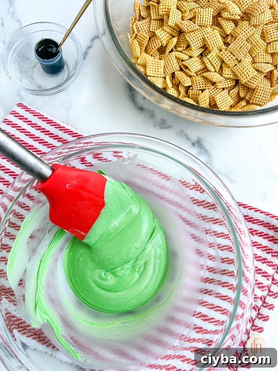Glass bowl with green colored chocolate being stirred by a red rubber spatula.