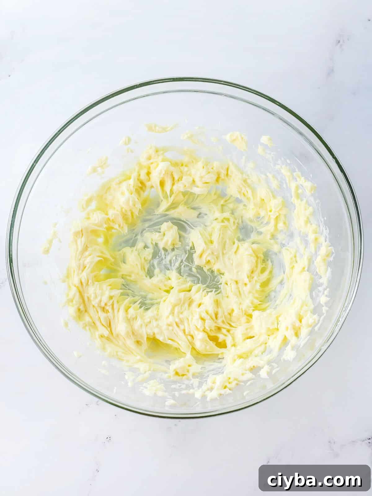 A glass bowl containing whipped or creamed butter on a white surface.