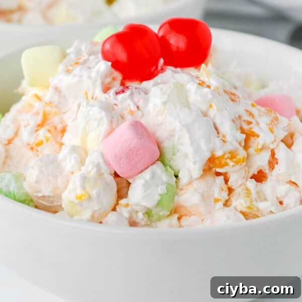 A bowl of ambrosia salad topped with two maraschino cherries, featuring whipped cream, fruit, and colorful mini marshmallows.