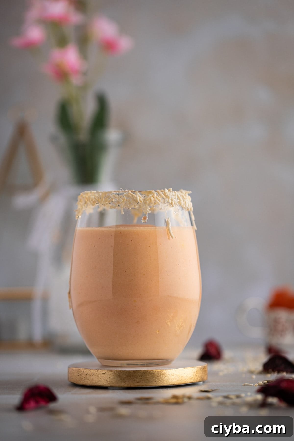 A light pink colored papaya smoothie in a large round glass, with the rim of the glass lined with shredded coconut.