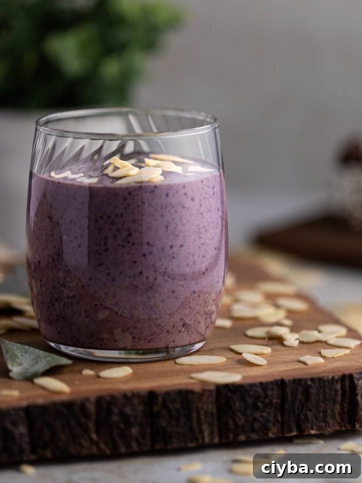 Up close view of a vegan blueberry tahini smoothie on a wooden board, with sliced almonds scattered on the table.