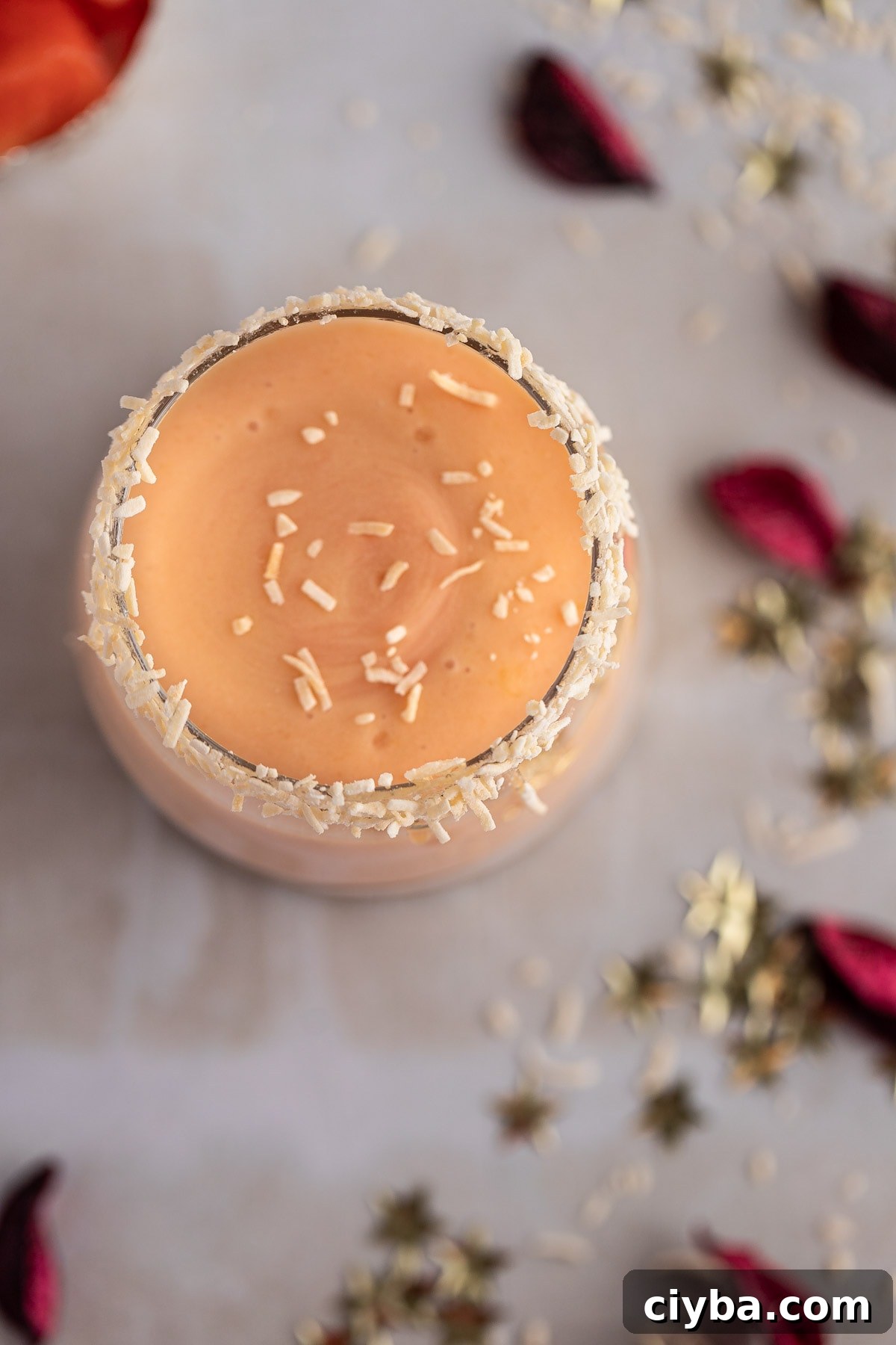 Overhead view of a orange papaya smoothie, topped with shredded coconut, on a marble table.