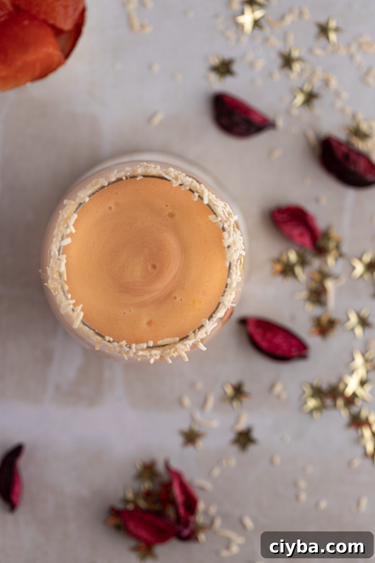 Overhead view of the smoothie on a light grey table, with pink petals and shredded coconut scattered on the table,