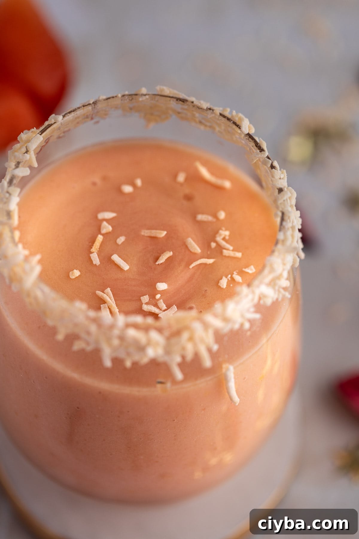 Up close view of the smoothie topped with shredded coconut, sitting on a white marble coaster.