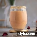 A light pink colored papaya smoothie in a large round glass, with the rim of the glass lined with shredded coconut.