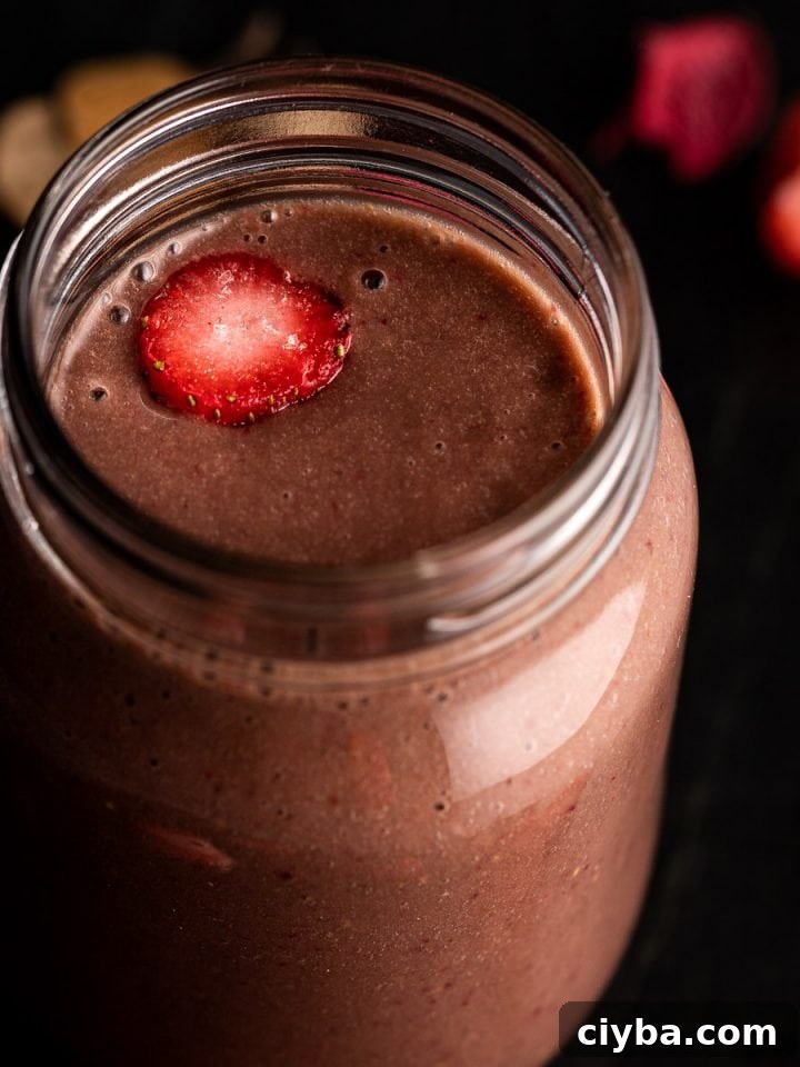 Close up view of a strawberry banana chocolate smoothie in a mason jar, on a black marble board.
