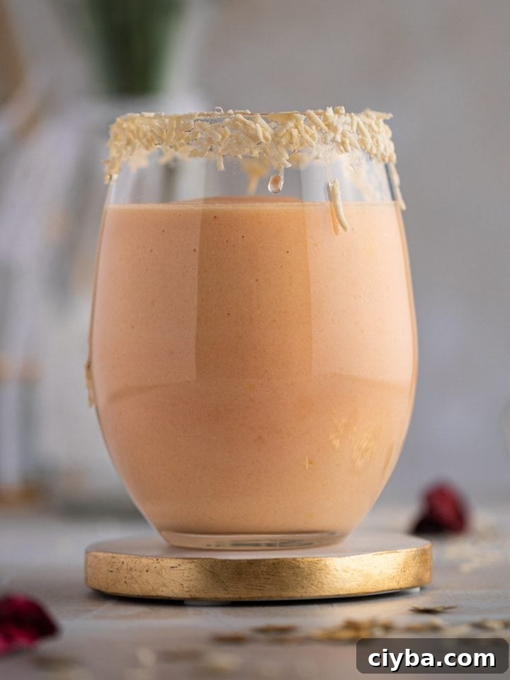 A light pink colored papaya smoothie in a large round glass, with the rim of the glass lined with shredded coconut.