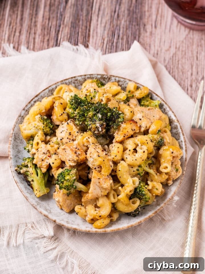 small plate with broccoli and chicken pasta with a gold fork and beige napkin
