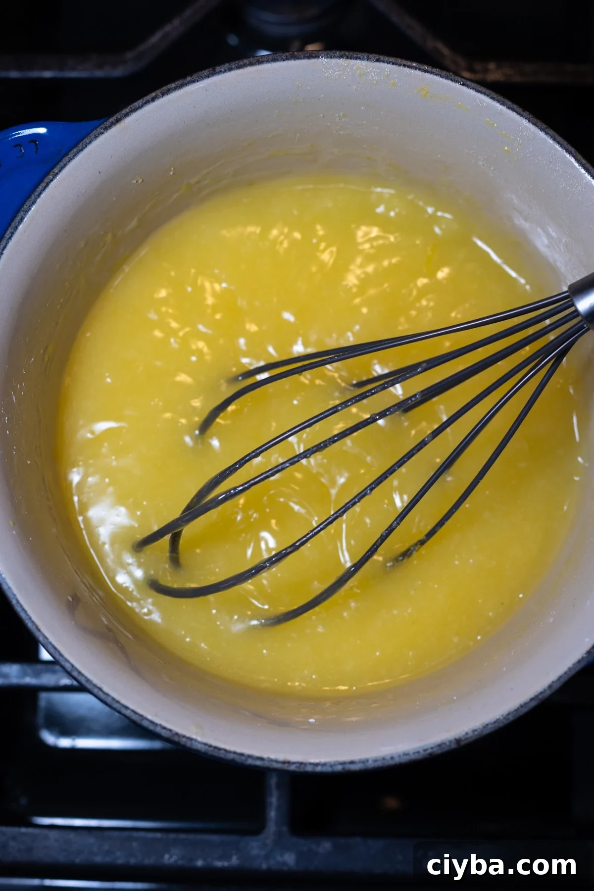 Person whisking lemon pie filling in a saucepan on the stovetop.