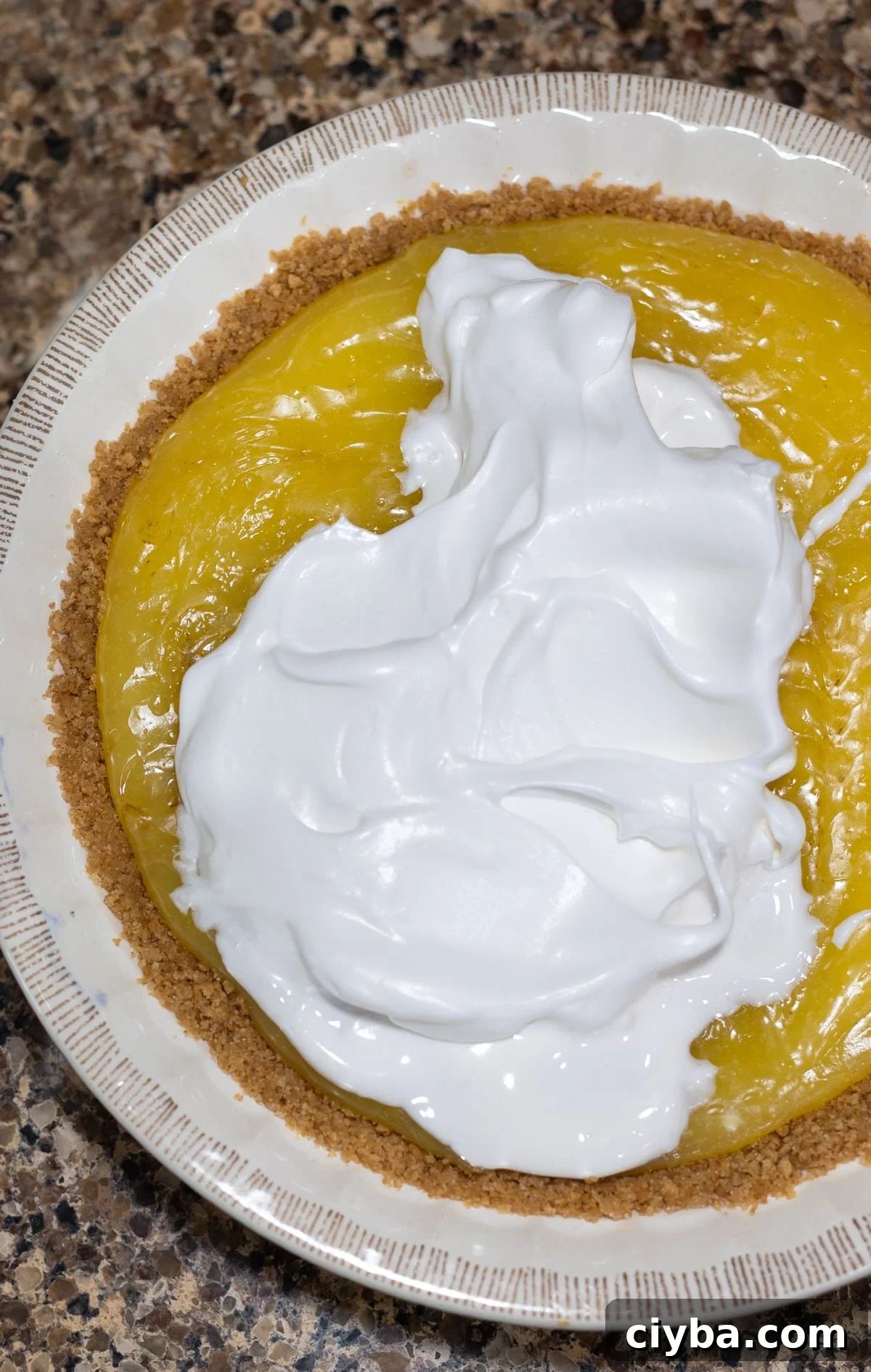 Person spreading meringue over lemon pie filling.