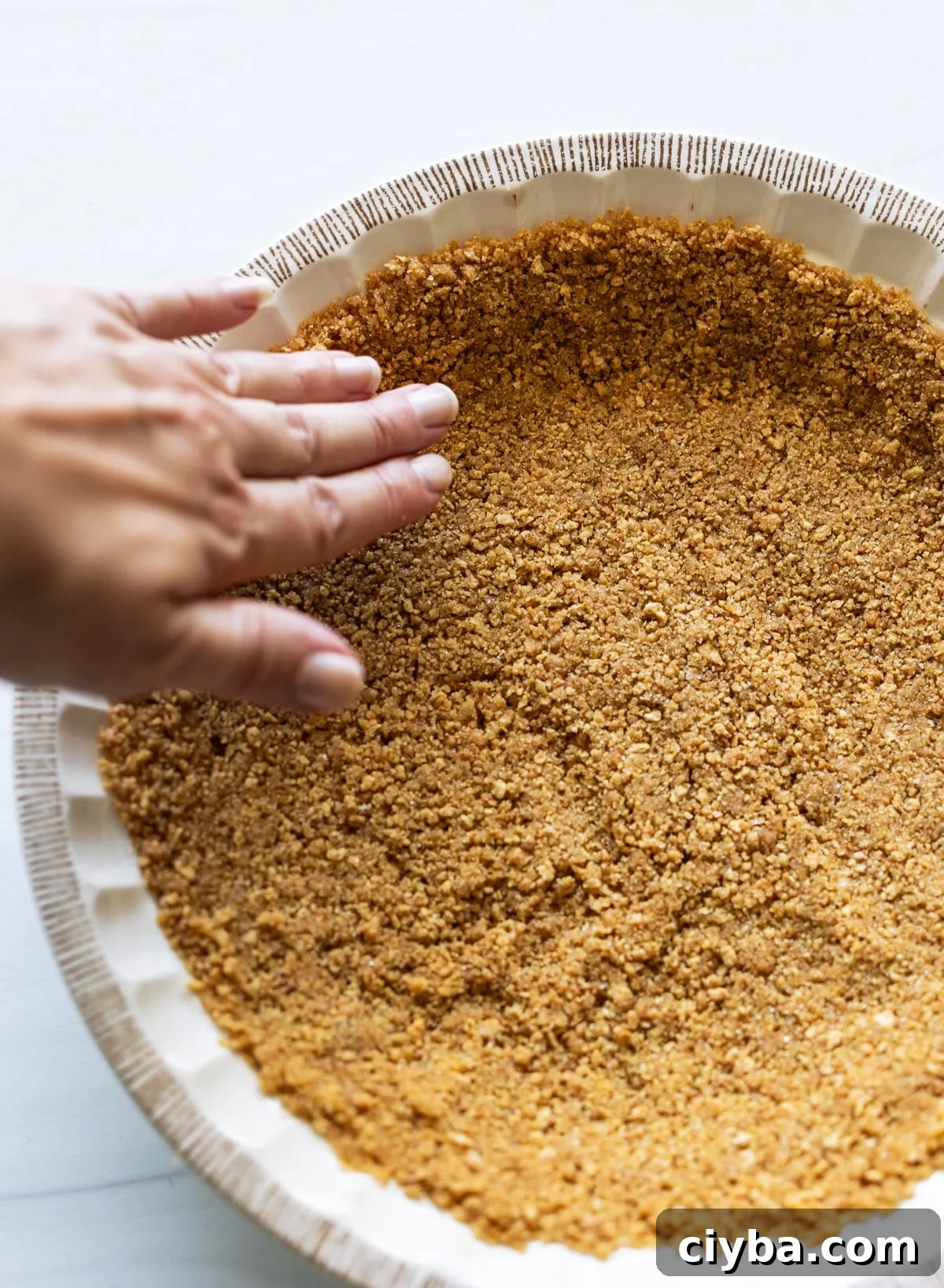 Person pressing down the graham cracker crust in the pie shell.