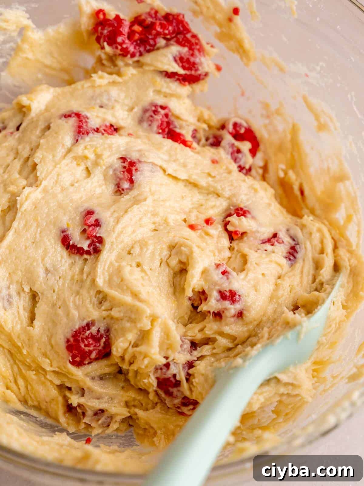 Lemon Raspberry Muffins with Zesty Lemon Glaze 8 Folding fresh raspberries into lemon muffin batter using a spatula.