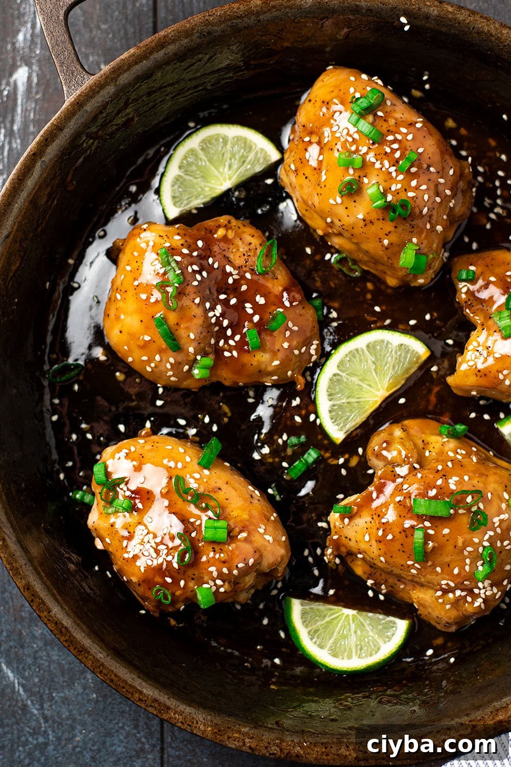 Roasted chicken thighs in a cast iron skillet topped with a sticky glaze and sesame seeds.