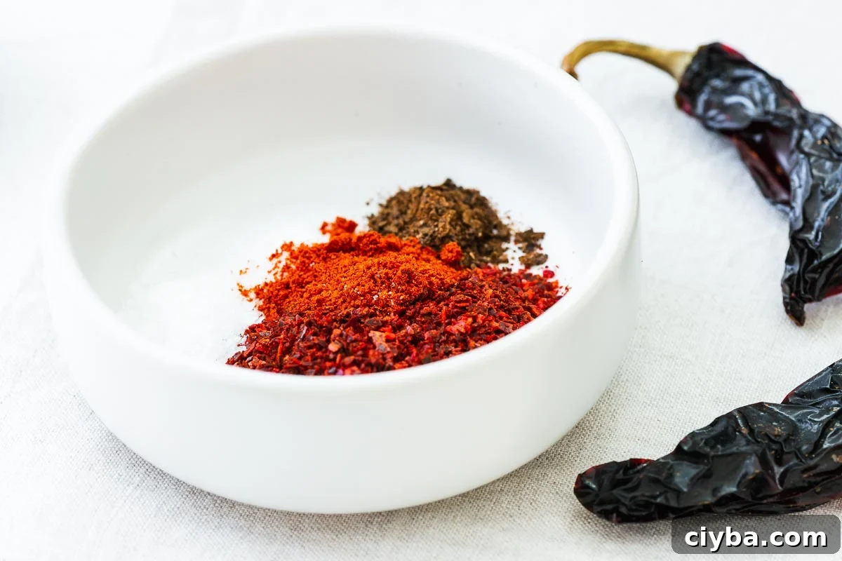Chilli flakes, smoked paprika, ground black lime, salt and citric acid in a small white bowl next to whole dried chillies.