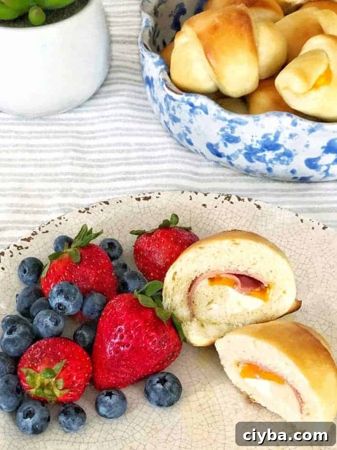 bowl of rolls and plate with cut open ham and cheese rolls and berries