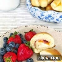 bowl of rolls and plate with cut open ham and cheese rolls and berries
