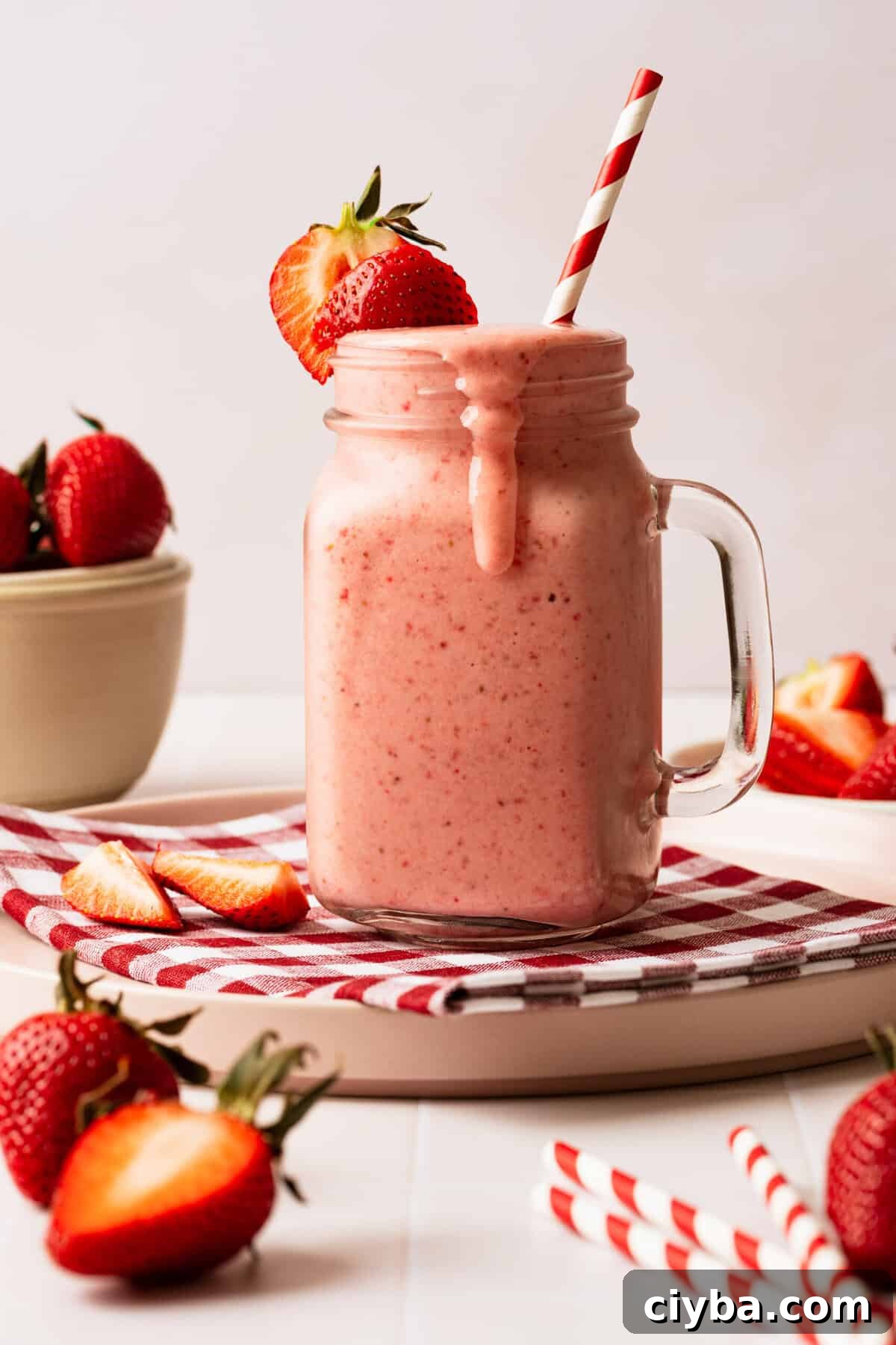 A strawberry milkshake in a glass mug with a straw in it.