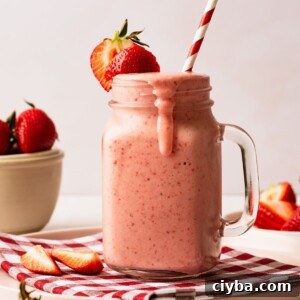 A glass filled with a strawberry milkshake with a straw in it.