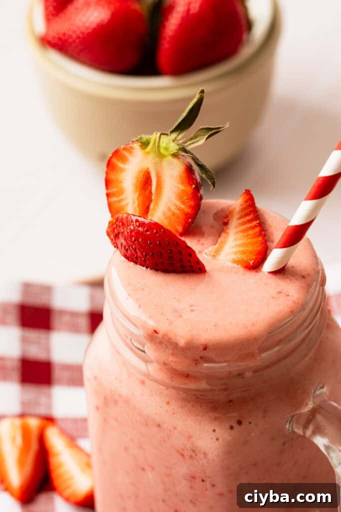 A glass filled with a strawberry milkshake with a straw in it.