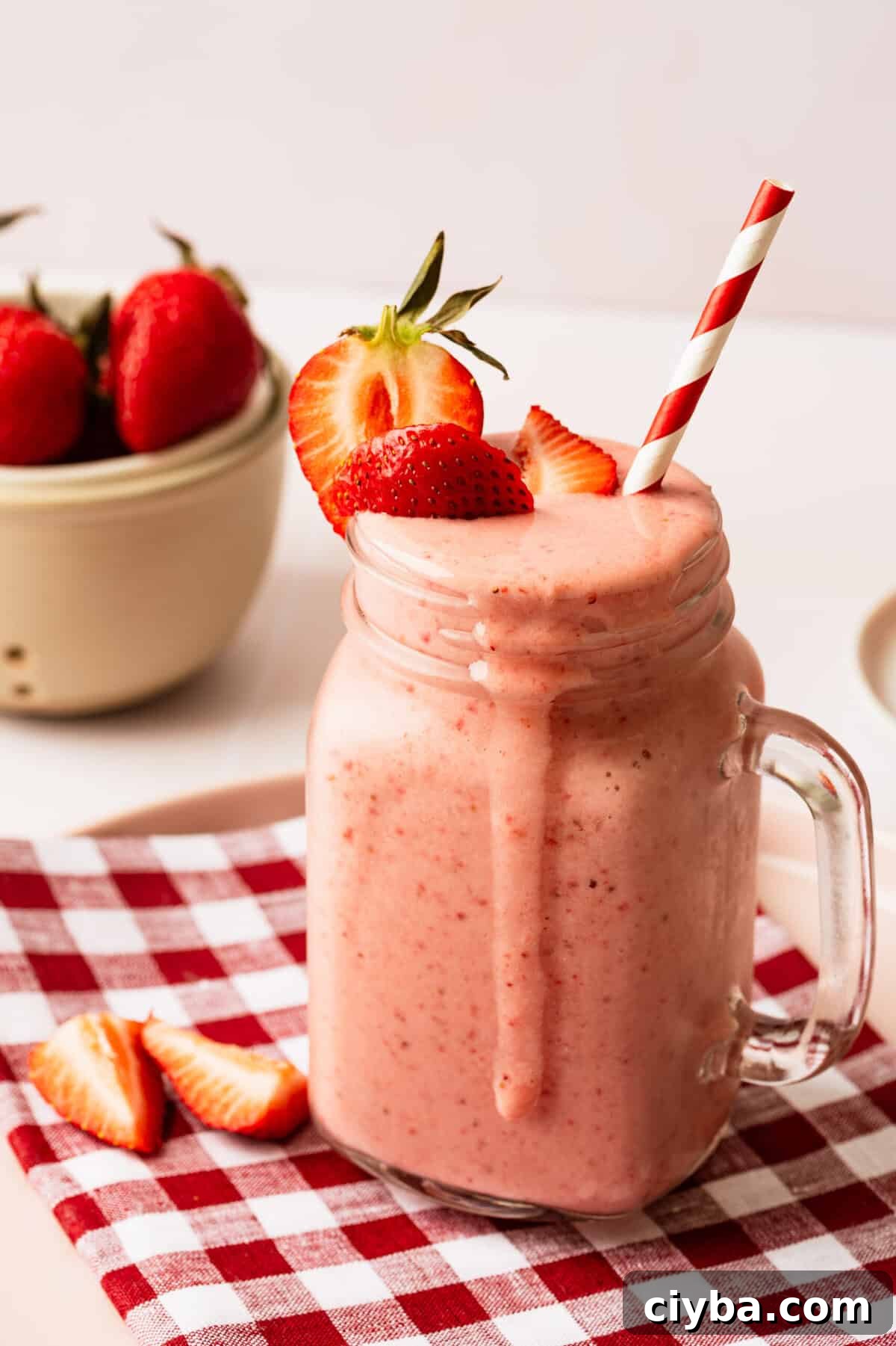 A strawberry milkshake in a glass mug topped with fresh strawberries.