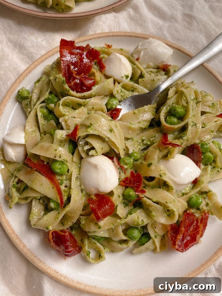 pesto pasta with prosciuttio, mozzarella, and peas on a plate with fork 