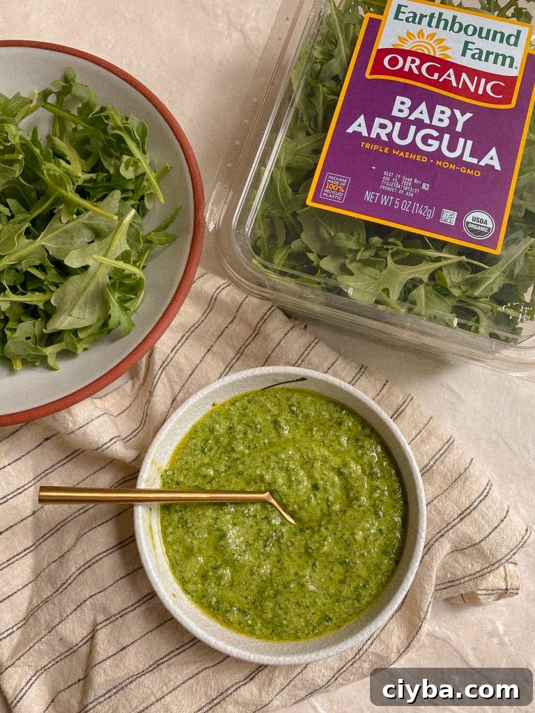 small bowl of arugula pesto with spoon and container of arugula and bowl of arugula