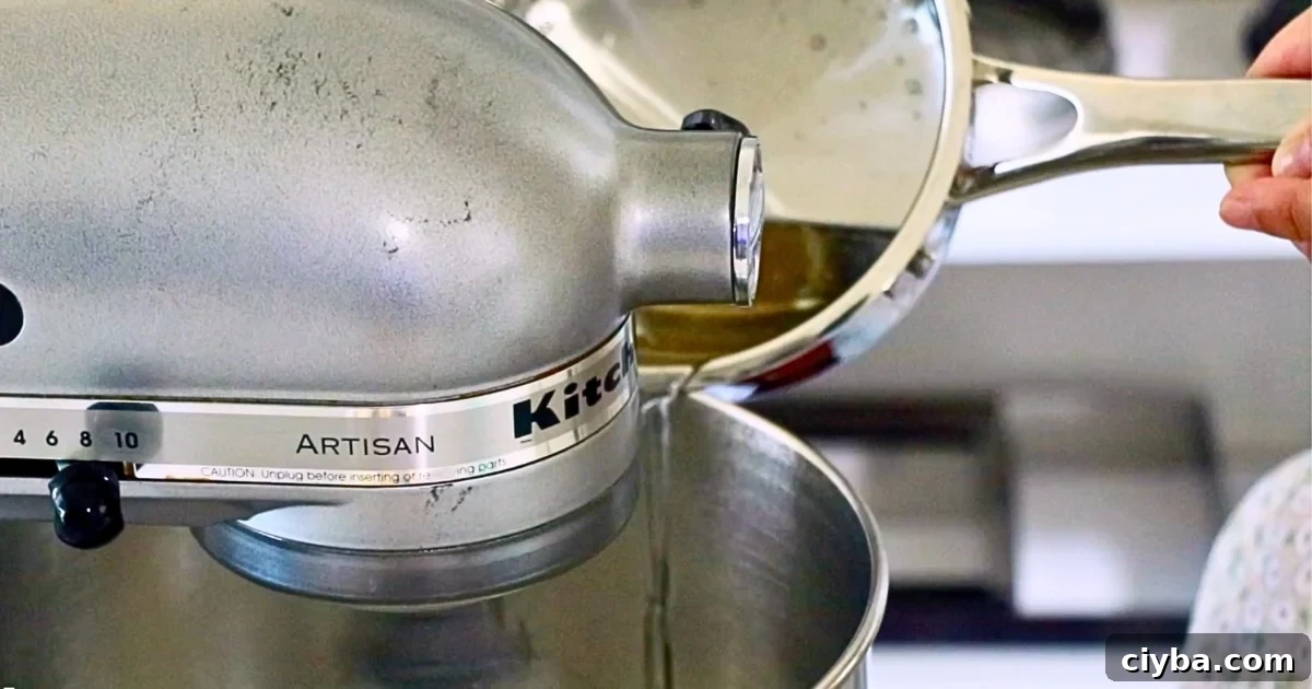pouring hot sugar syrup into the stand mixer of meringue to make Italian meringue
