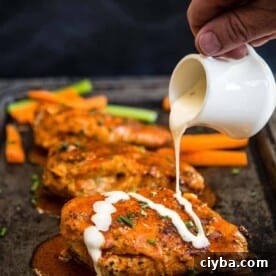 Buffalo stuffed chicken breasts on a platter with ranch being drizzled over the top.
