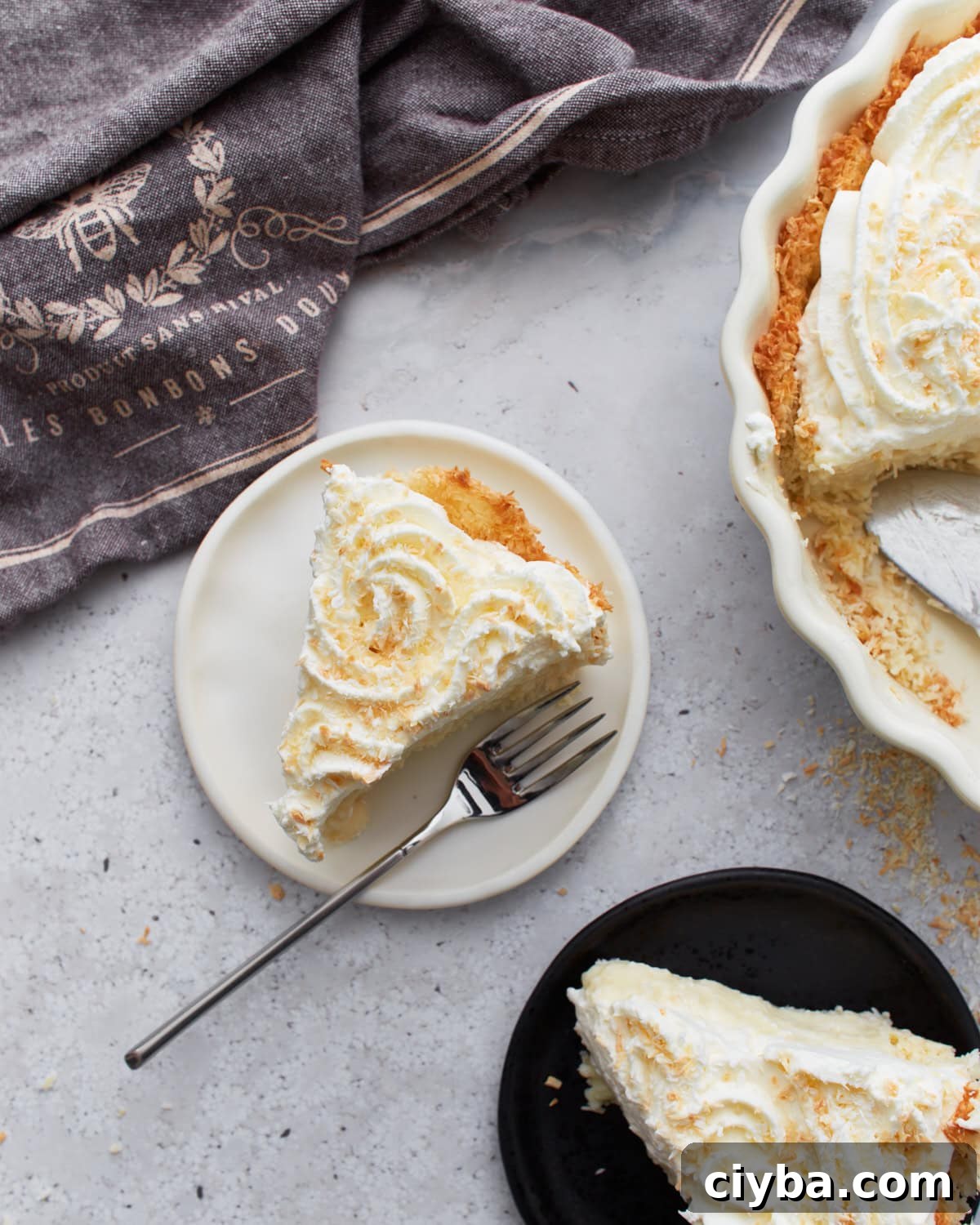 Slice of gluten-free coconut cream pie on a white plate with a fork, next to a full pie topped with whipped cream and toasted coconut.